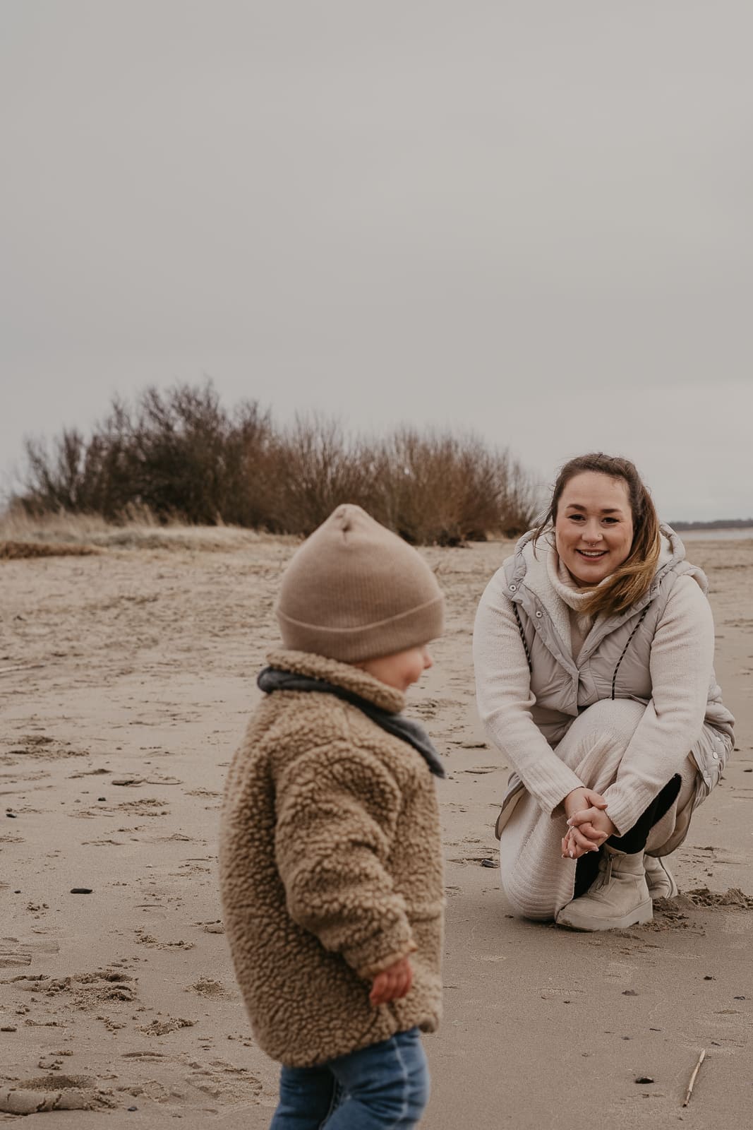 mutter kniet sich zu ihrem kind hinunter bei befinden sich am strand es ist kalt