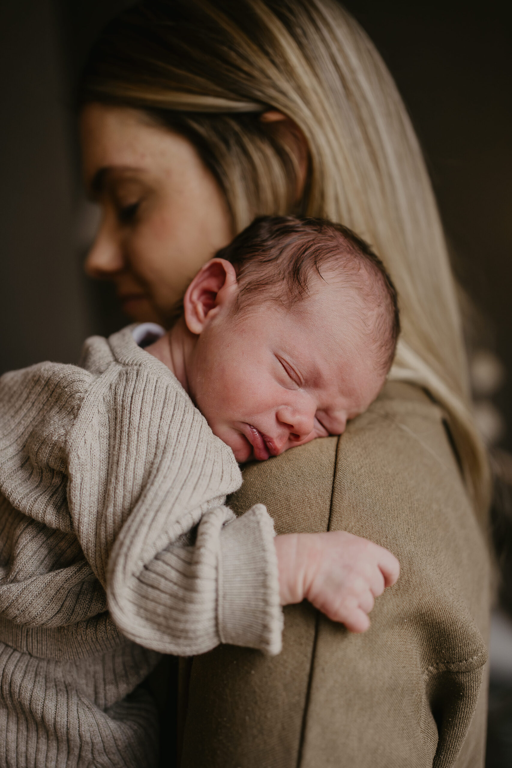 mutter die Ihr neugeborenes Kind auf der Schulter trägt. beide haben die Augen geschlossen und sind in erdtoenen gekleidet.